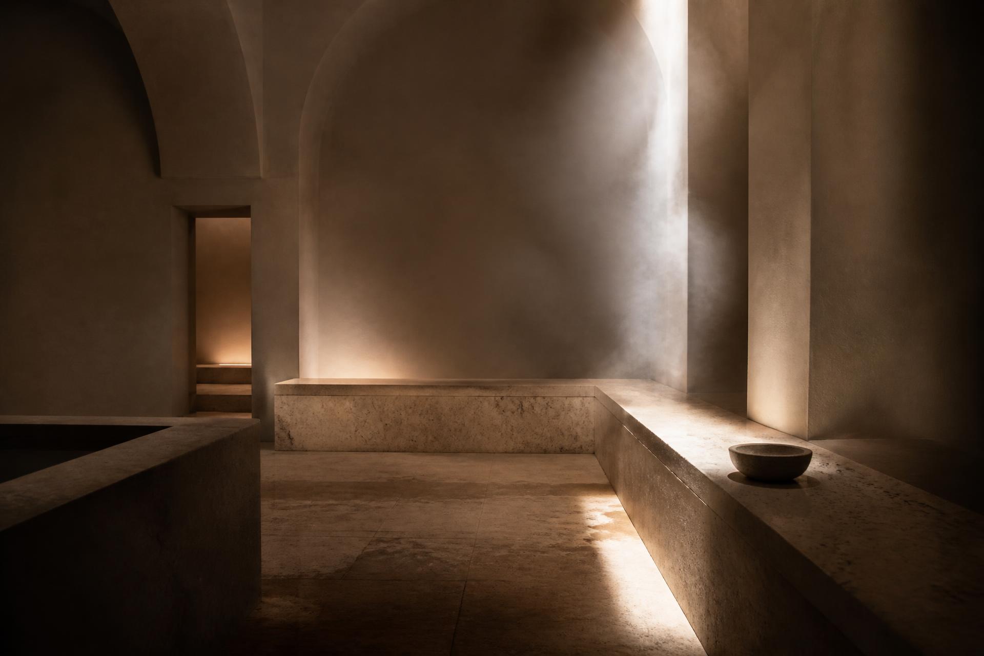 Empty stone bathhouse interior with a shaft of natural light falling across a travertine bench